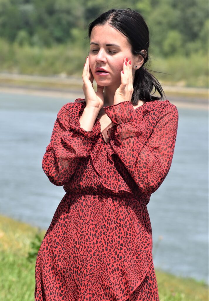 a woman in a red dress holding her hand to her face