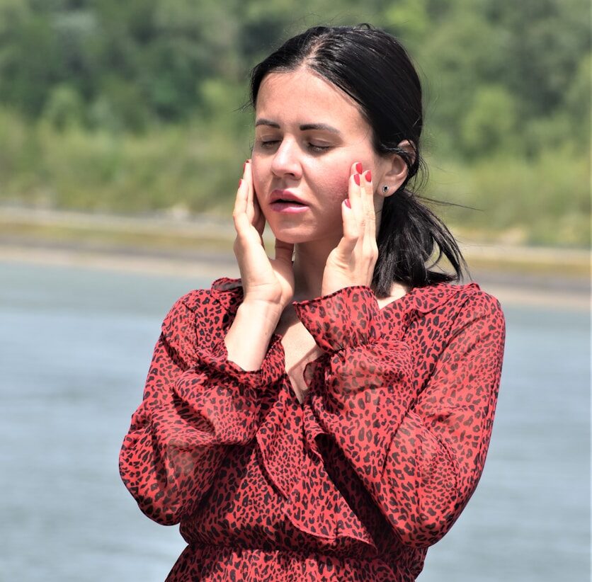 a woman in a red dress holding her hand to her face